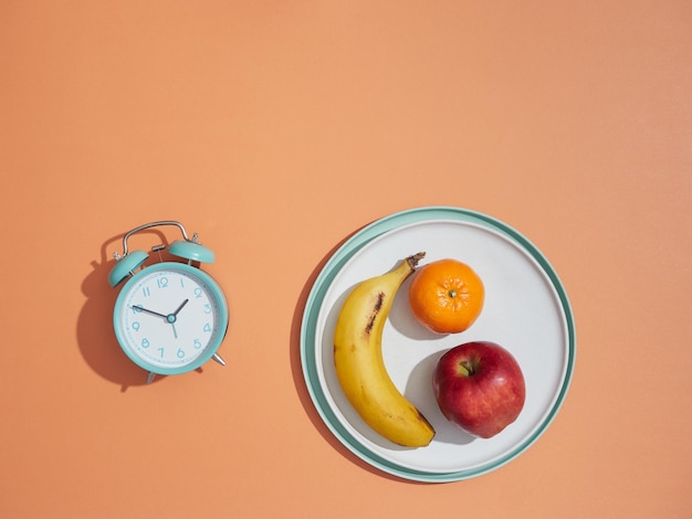 Maaltijd wekker en fruit in een bord Gezond eten concept diëten gewichtsverlies en intermitterend vasten Bovenaanzicht kopie ruimte oranje achtergrond