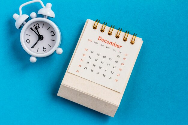 Maandelijkse tafelkalender voor december 2023 en wekker op een blauwe achtergrond