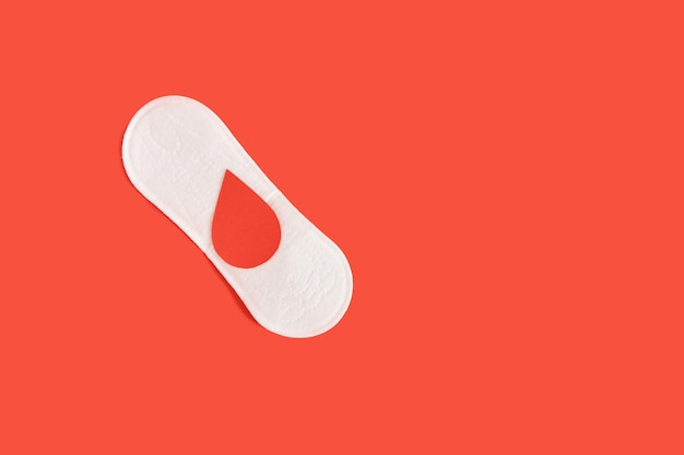 Maandverband en een druppel bloed van papier op een rode achtergrond, menstruatieconcept