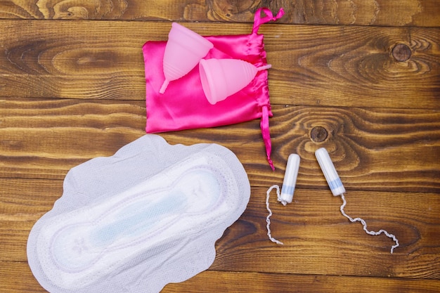 Maandverband tampons en menstruatiecups op houten achtergrond Bovenaanzicht Concept van kritieke dagen menstruatie vrouwelijke hygiëne