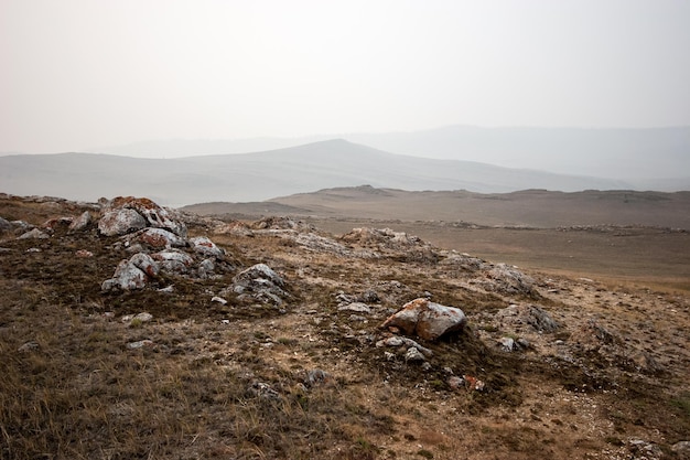 Maanlandschap in de steppe met heuvels en stenen op een mistige ochtend Grijze lucht Oud gras op de grond Rond en op de stenen is rood mos Ruimte kopiëren