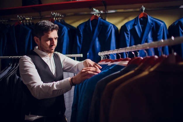 Maatwerk, maatwerk. Herenpak, kleermaker in zijn atelier. Elegante man kostuums die in rij hangen. Luxe heren klassieke pakken op rek in elegante herenboetiek.