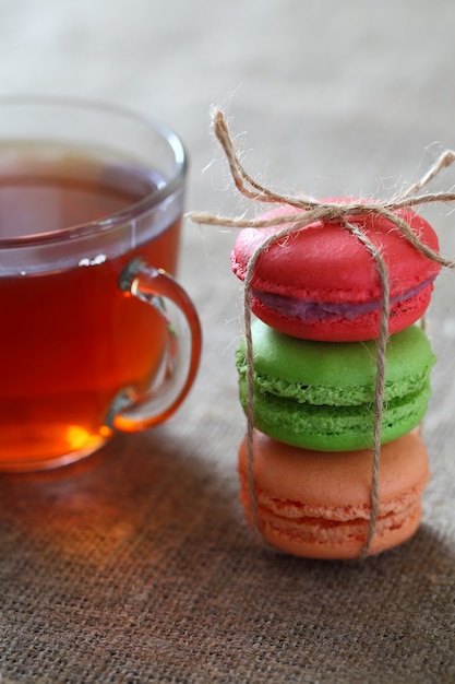 Macaron three pieces red, green and orange tied with rope and a mug with tea on burlap tablecloth. Vertical frame.