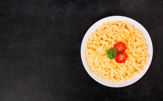 Macaroni and cheese on a white plate with parsley and cherry tomatoes on a black background
