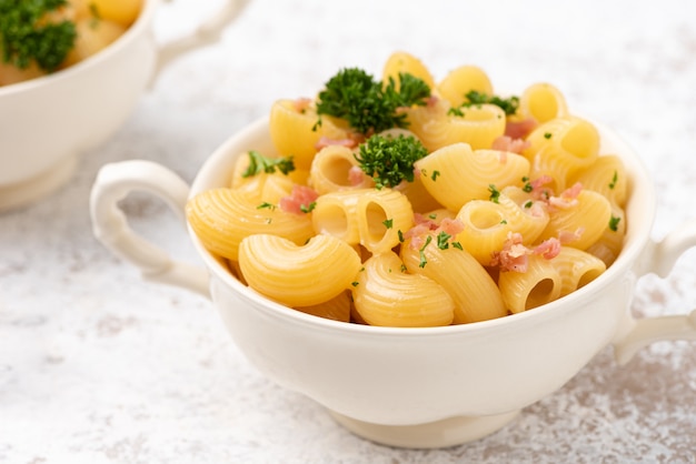 Macaroni cheese with bacon on white surface