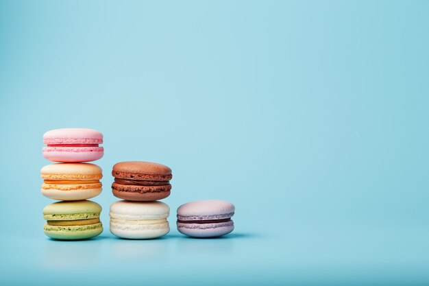 Macaroni cookies of different colors are arranged in the shape of pyramid steps on a blue background.