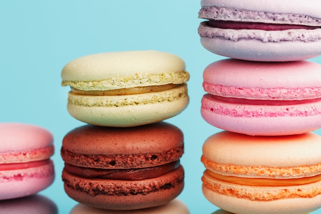 Macaroni cookies of different colors are arranged in the shape of pyramid steps on a blue background.