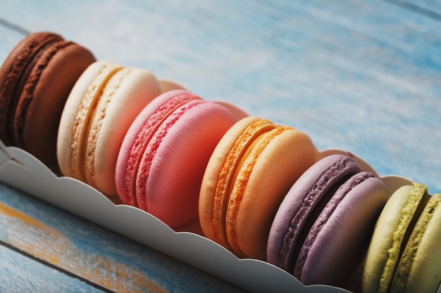 Macaroni cookies of different colors in a box on a blue, old wooden background of blue color.