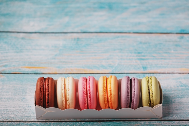 Macaroni cookies of different colors in a box on a blue, old wooden background of blue color.