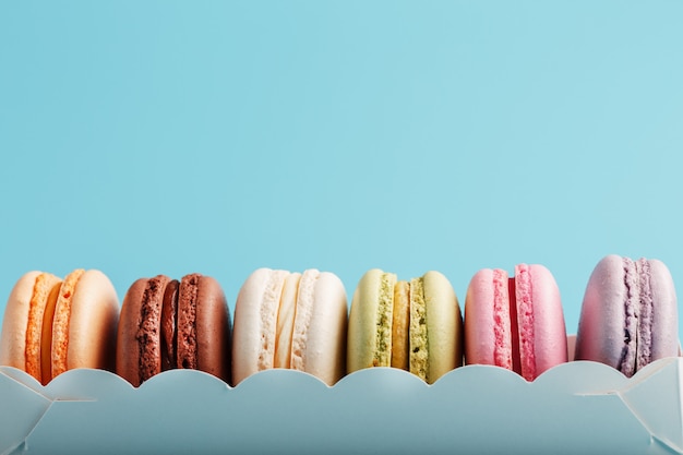 Macaroni cookies van verschillende kleuren in een witte doos op een blauwe achtergrond.