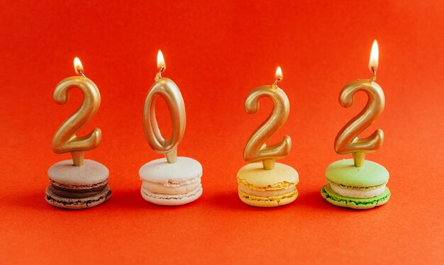 Photo macarons with burning candles 2022 on red background. new year.