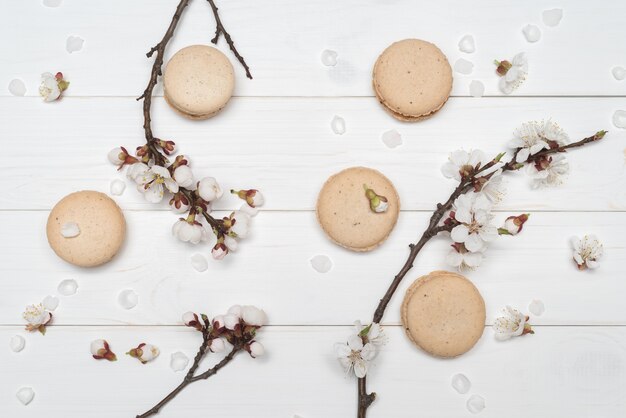 Macaroon cookies and flowers on white wooden background