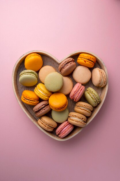 Macaroons colorful cookies in wooden heart bowl Macarons french sweet dessert top view pink background Copy space