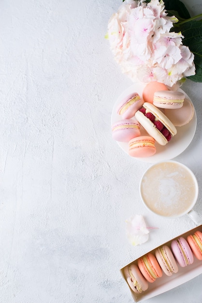 Macaroons and cup of coffee with flowers over white texture