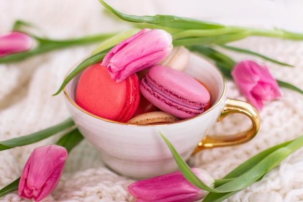 Macaroons in golden mug and pink tulips