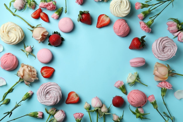 Macaroons, marshmallows, flowers and strawberry on blue background