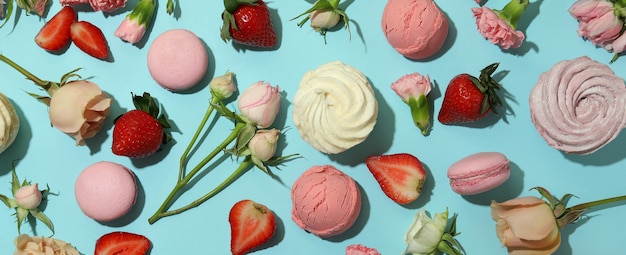 Macaroons, marshmallows, flowers and strawberry on blue background