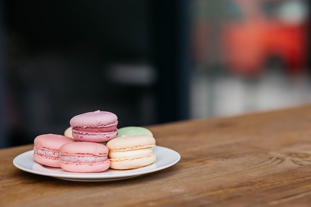 Macaroons in a plate on a background of cafes macaroons on a\
wooden table