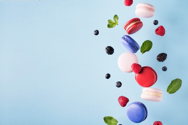 Macaroons, raspberries, blackberries and blueberries flying over blue