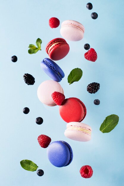 Macaroons, raspberries, blackberries and blueberries flying over blue