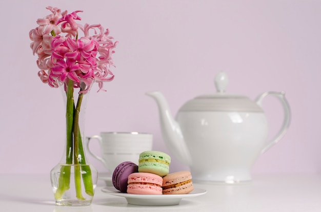 Macaroons and transparent vase with pink hyacinth flowers on porcelain tea pot and cup 
