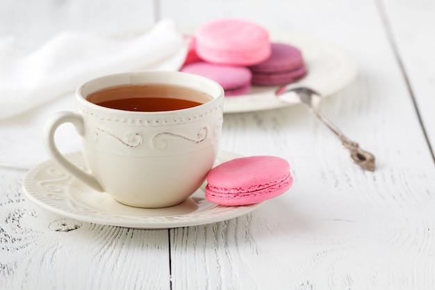 Macaroons with hot tea on wooden table.