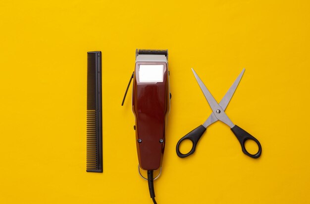 Machine for haircuts scissors and comb on yellow background\
barbershop hair clipper top view flat lay