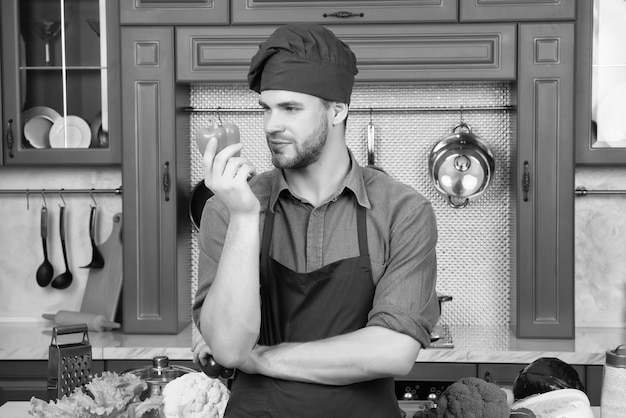 Macho chef in red hat apron look at orange pepper