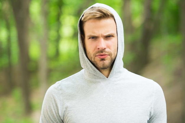 Macho man. man in hood. casual style. male fashion. unshaven
guy outdoor. seriousness and masculinity. sportswear fashion.
sportsman relax after training outdoor. handsome unshaven man in
hood.