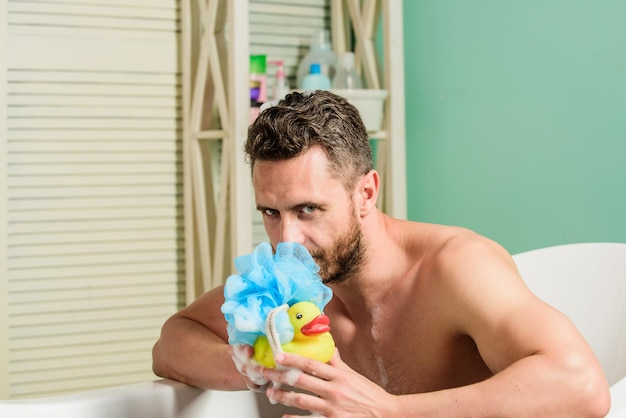 Macho naked in bathtub funny duckling playful mood macho enjoy bath Sexy man in bathroom Sex and relaxation concept man wash muscular body with foam sponge Wash off foam with water carefully