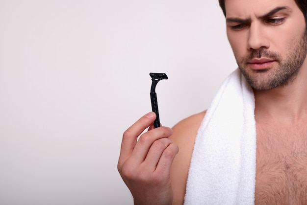 Photo macho with black razor in hand and white towel in shoulder