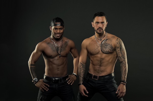 Machos with muscular tattooed torsos look attractive dark background Athletes on confident faces with nude muscular chests Guys sportsmen with sexy muscular torsos Masculinity concept