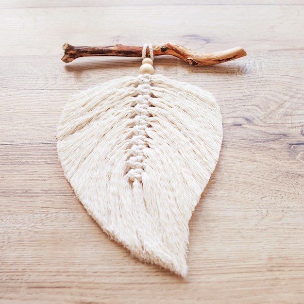 Macrame leaf in natural color on a wooden table Cotton rope decor macrame to make your room more cozy and unique Woman hobby Handmade wall hanging decor Close up image