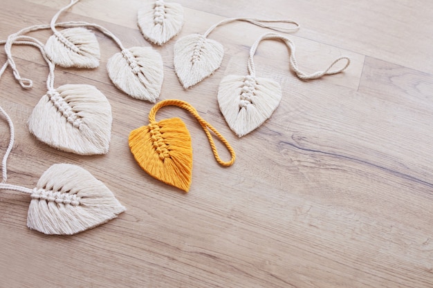 Macrame leaves in yellow  and natural color on the wooden background. Cotton rope decor macrame to make your home more cozy and unique.