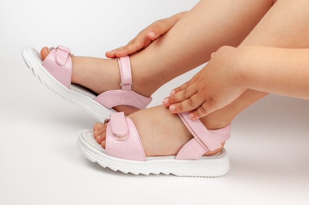 Macro details pink childrens sandals on the girls feet of a child sitting on a white poured background