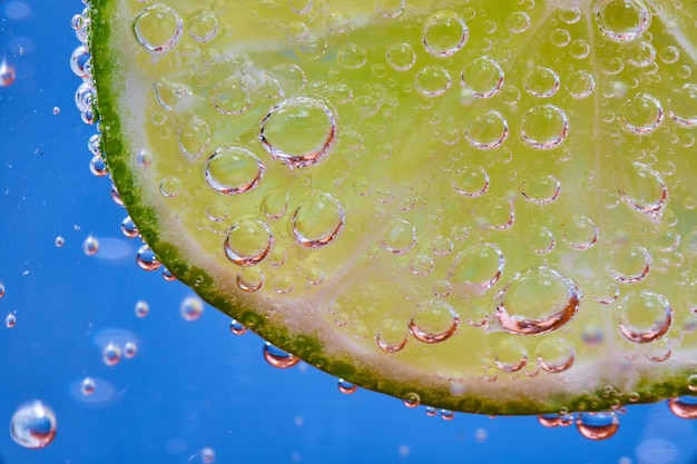 Macro of fizzy bubbles on lime slice against blue background