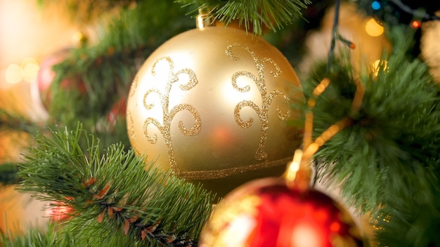 Macro image of glittering and sparkling golden Christmas bauble hanging on Xmas tree branch at house living room