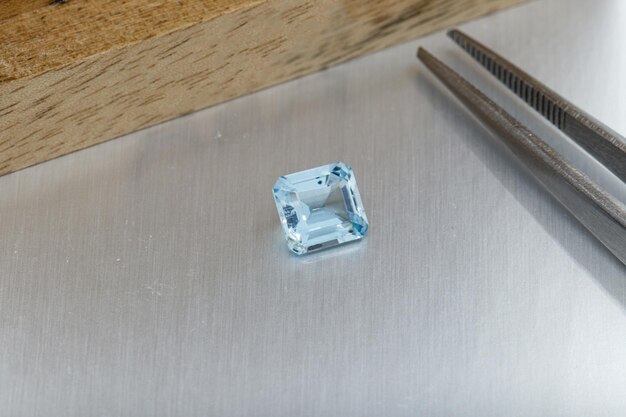 Macro mineral faceted stone aquamarine with tweezers on a gray background