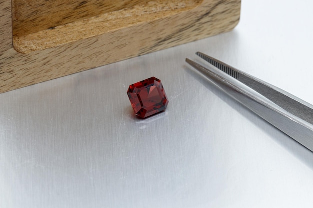 Macro mineral faceted stone Garnet with tweezers on a gray background