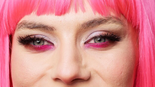 Macro-opname van een aantrekkelijke vrouw met mooie oogmake-up en roze haar poserend in de studio, plezier hebbend en zelfverzekerd. Gezond positief schoonheidsmodel met grote wimpers. Extreem dichtbij.