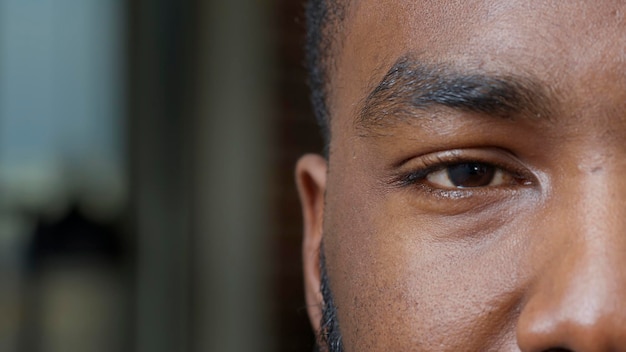 Macro-opname van een Afro-Amerikaanse man die één oog op de camera toont en voor hem kijkt. Authentieke volwassene met de helft van het gezicht met wenkbrauw en wimpers, natuurlijke huid en gefocuste blik. Detailopname.