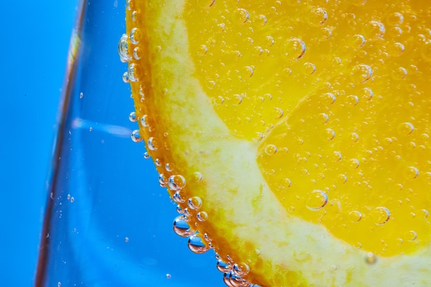 Macro of orange slice covered in bubbles inside clear glass with blue background