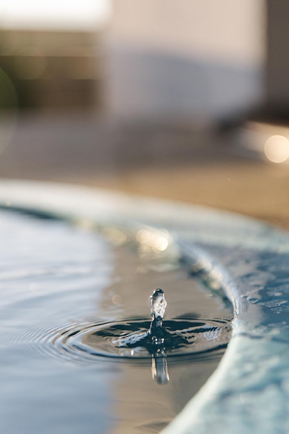 Макрофото капель воды капает в чистый бассейн с голубой водой, отражающей рябь солнца
