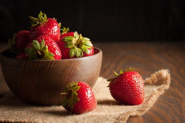 Macro photo of fresh ripe red strawberry in a wooden bowl on rustic background. Organic natural products.