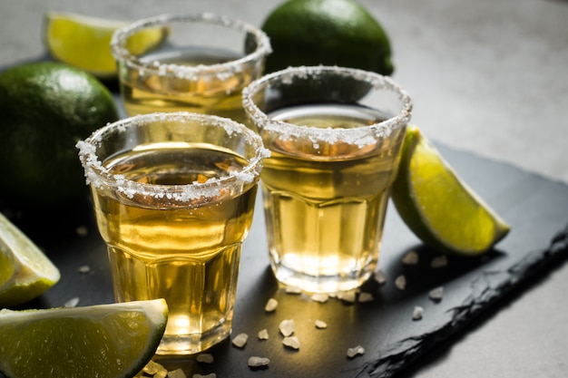 Macro photo of shots of gold Mexican tequila with lime and salt on wooden rustic background. Alcoholic drink concept. selective focus.