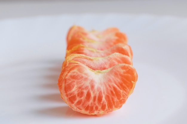 Macro photo slices in a white plate close up several pieces of mandarin lie on the table background out of focus