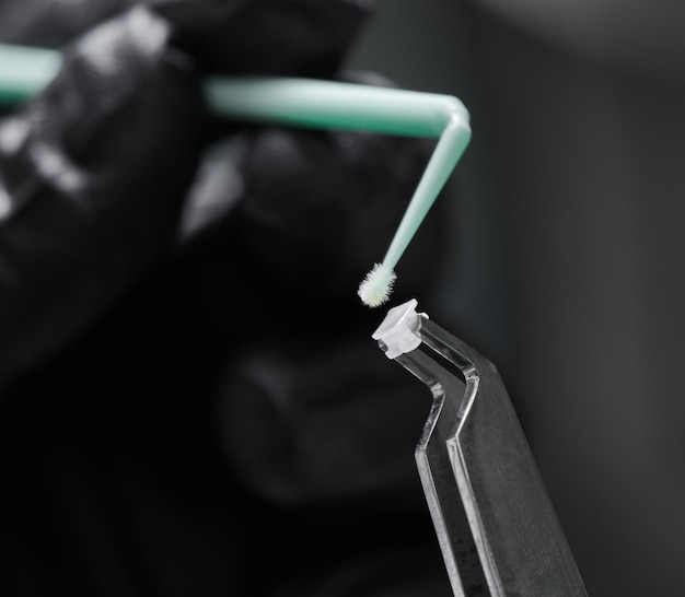 Photo macro shooting of orthodontic bracket steel dental forceps with ceramic bracket and a hand with a tiny colorful brush in focus on dark background orthodontic accessories concept