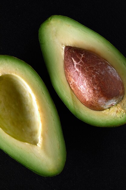 Macro shot of fresh avocados cut in a half on the black background.