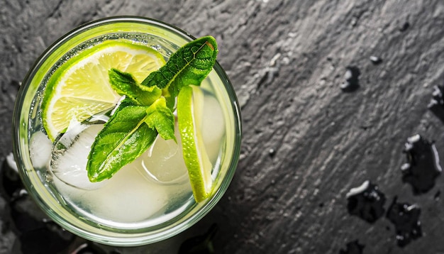 Macro shot glass of mojito with sliced lime and mint on black stone surface top view