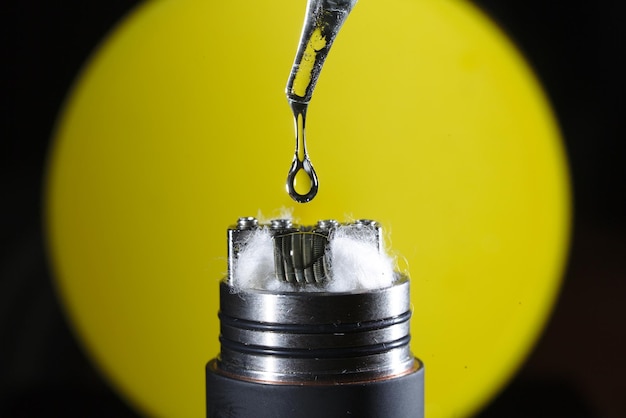 Photo macro shot of liquid drop on electronic cigarette against yellow background